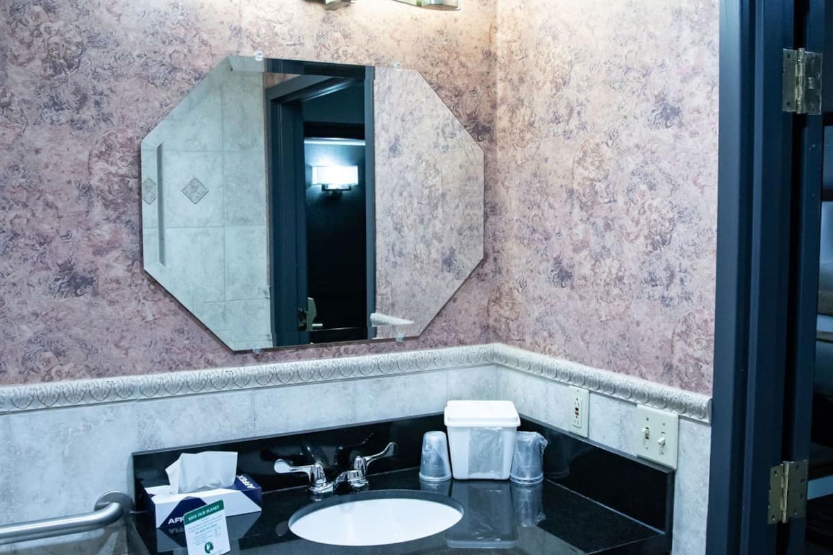 Un baño con un lavamanos negro, un espejo y un cesto de basura.