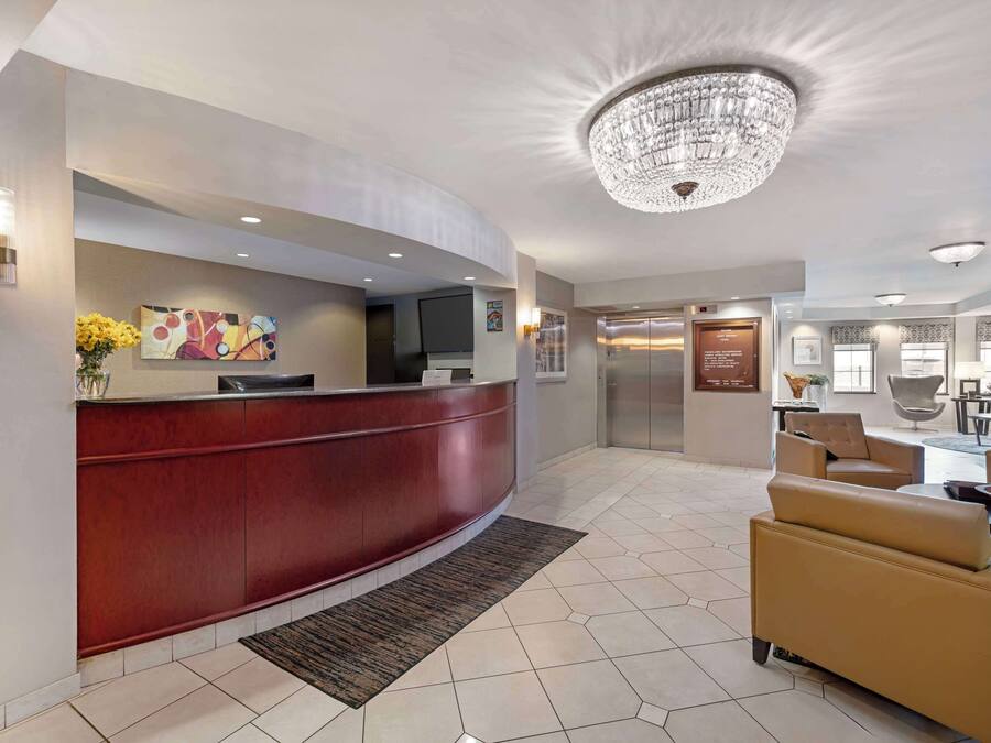 A hotel lobby with a curved reception desk, a chandelier, a seating area with leather chairs, and a tiled floor.