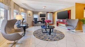 Un hall d’hôtel moderne avec une table basse ronde, deux fauteuils gris, un téléviseur et un comptoir d’accueil.