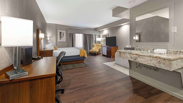 Une chambre d’hôtel équipée d’un lit, d’un bureau, d’une chaise, d’une télévision et d’une salle de bain avec un lavabo et un miroir.