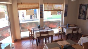 A restaurant interior with tables set for dining, large windows with blinds, and a view of the street outside. - Hotel Catedral Casa Cornejo (Alajuela)
