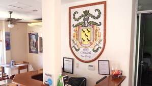 A reception desk with a framed coat of arms, a digital clock, and a Payless gas station sign. - Hotel Catedral Casa Cornejo (Alajuela)