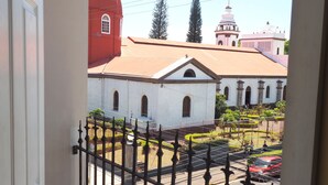 A view of a church with a dome and a bell tower, a street with cars, and a fenced garden area. - Hotel Catedral Casa Cornejo (Alajuela)