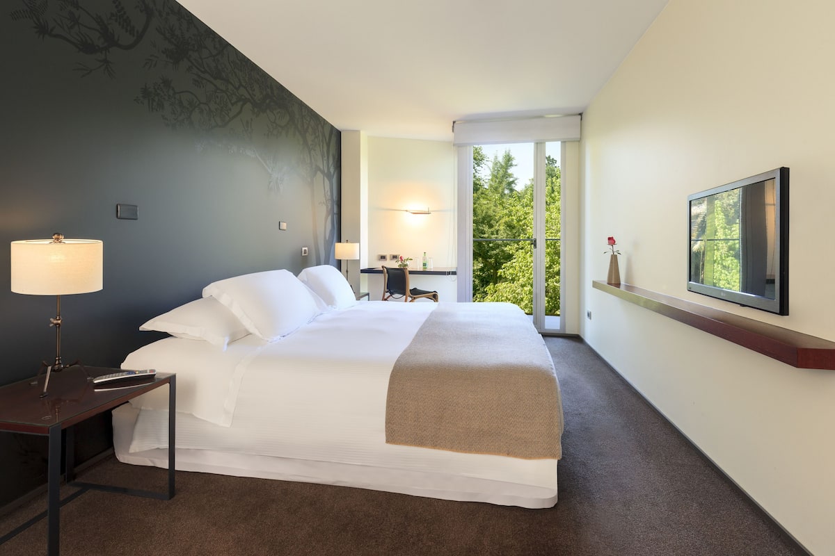 Une chambre d’hôtel avec un grand lit, des lampes de chevet, un bureau et un téléviseur fixé au mur.