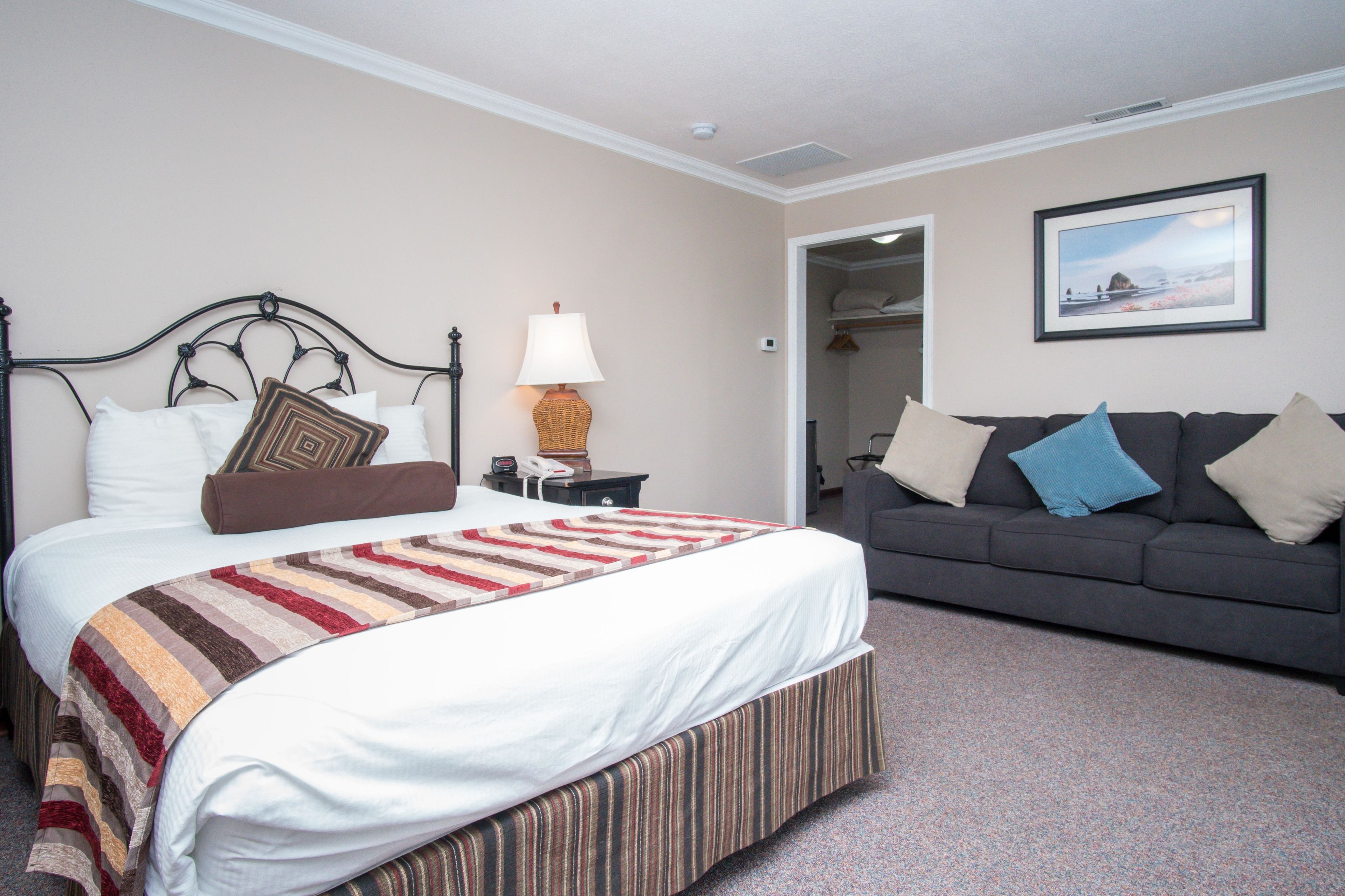 A hotel room with a bed, a sofa, a lamp, and a framed picture on the wall.