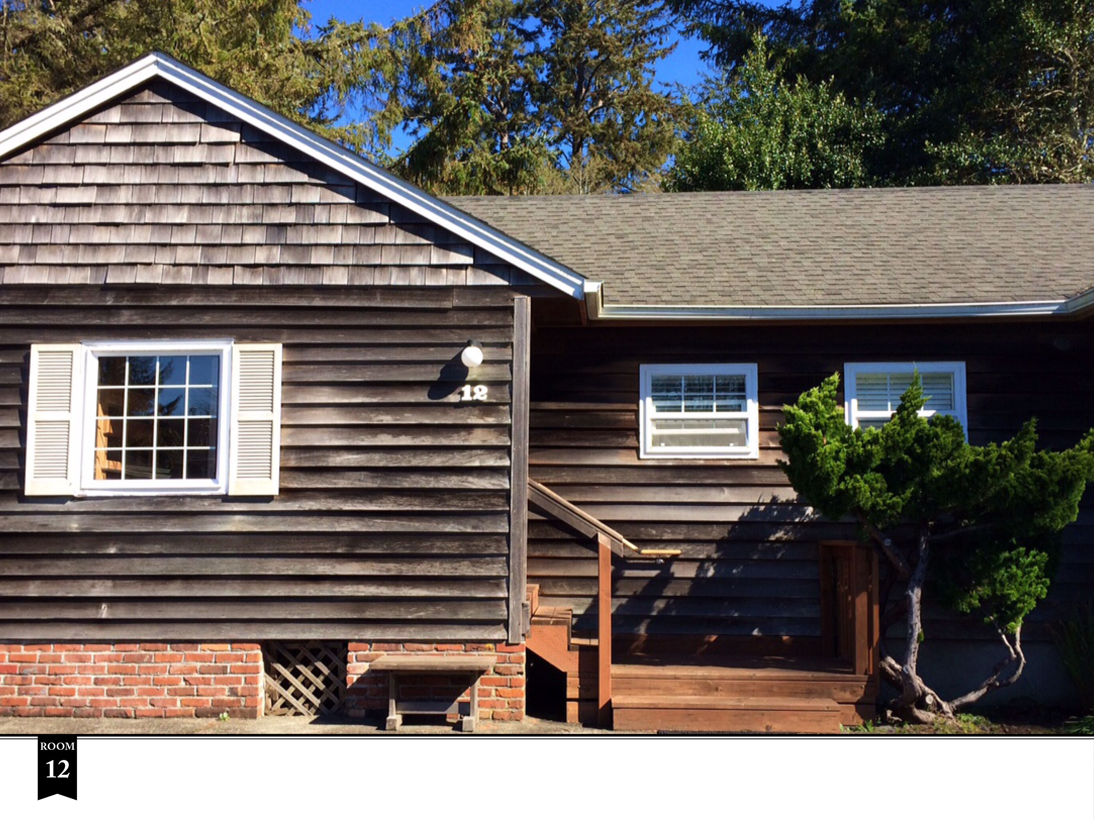 A two-story house with a wooden exterior, a brick foundation, and a small porch.