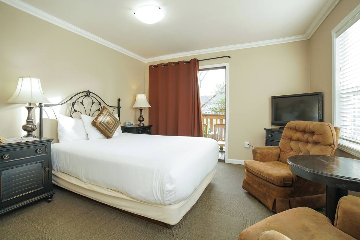 Une chambre d’hôtel comprenant un lit, deux tables de chevet avec des lampes, une chaise, une petite table et un téléviseur.