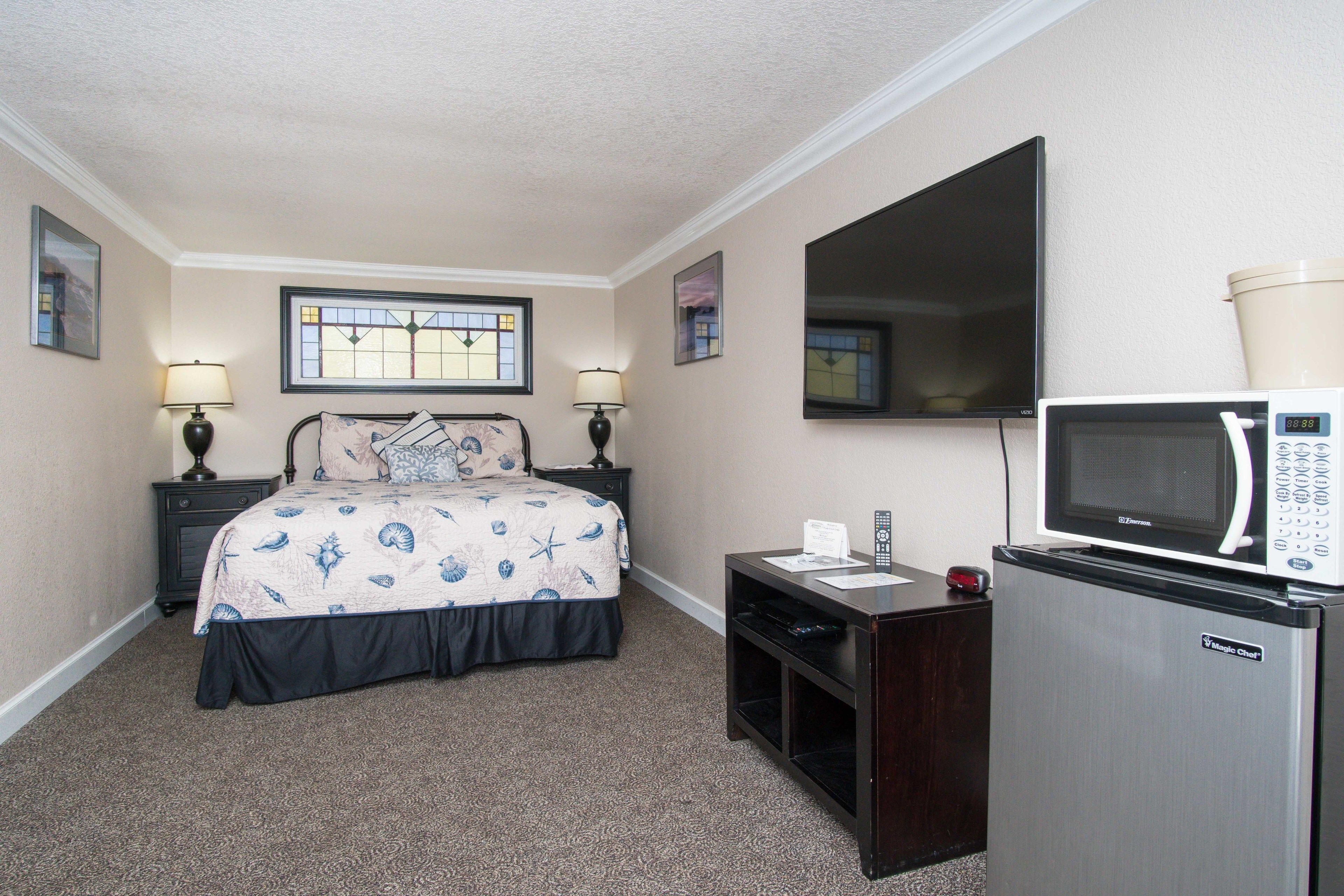 Habitación de hotel con cama, televisor, microondas y escritorio con lámpara.