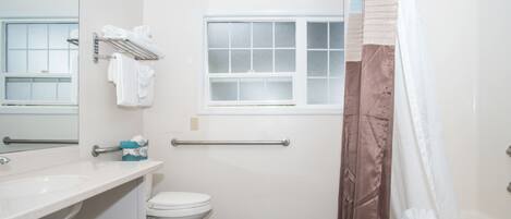A bathroom with a white sink, toilet, and a window with frosted glass. There is a towel rack with folded towels and a hand dryer.
