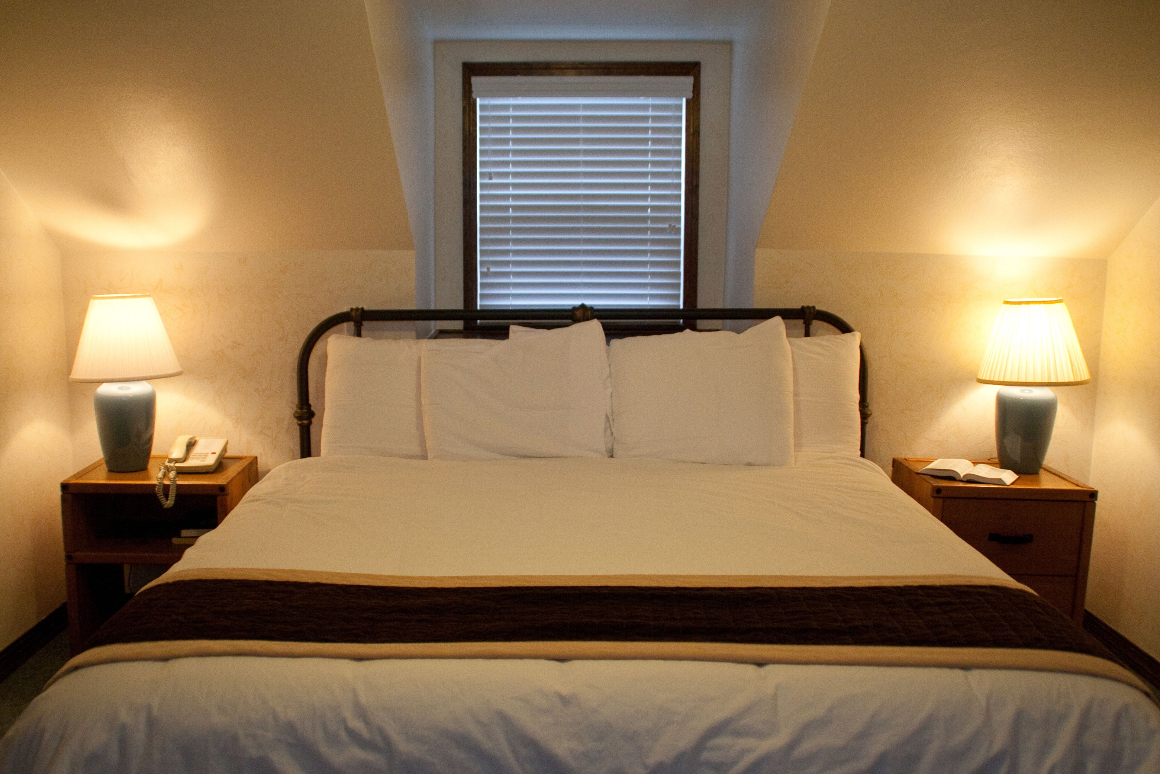 A neatly made bed with white linens, two bedside tables with lamps, and a window with blinds.