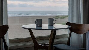 A table with two mugs and a view of the beach through a window. - The Ocean Front at Seaside (Seaside)
