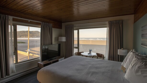 A hotel room with a large bed, a TV, a small table with a bottle, and a view of the beach. - The Ocean Front at Seaside (Seaside)