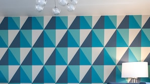 A room with a geometric patterned wall, a blue armchair, a red ottoman, a round grey ottoman, and a modern chandelier. - The Ocean Front at Seaside (Seaside)
