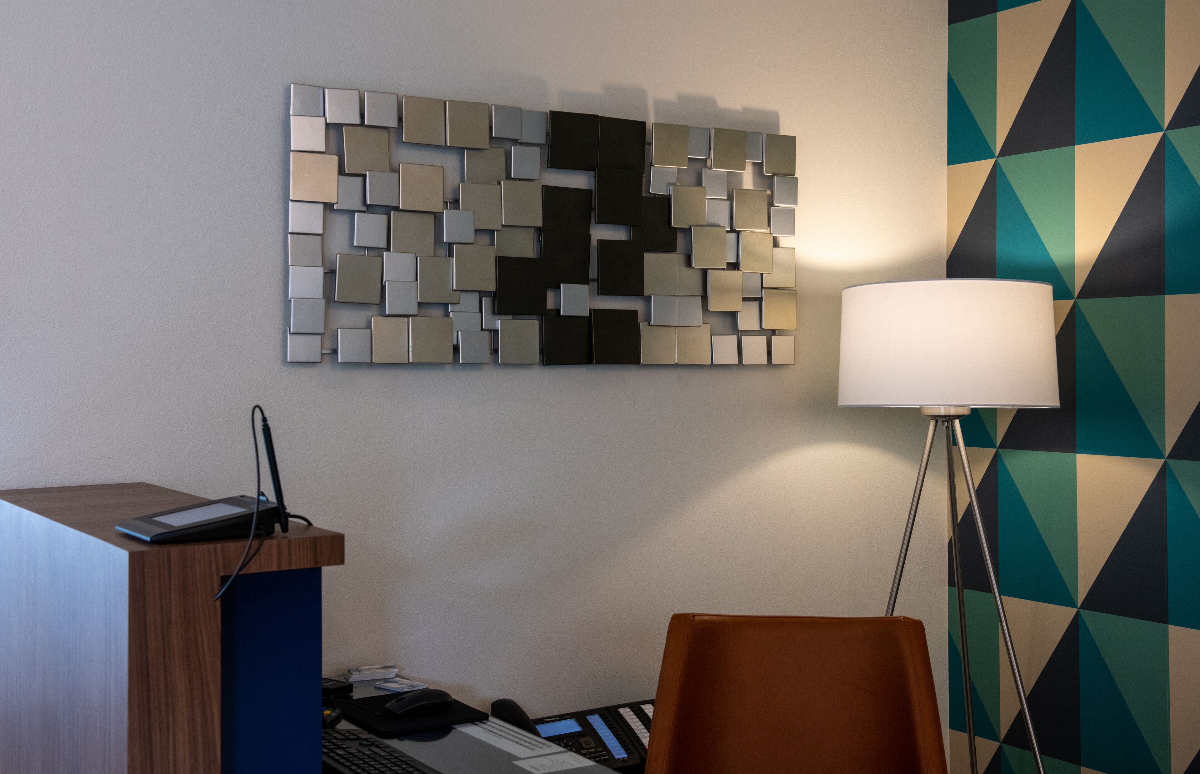 Una habitación de hotel con una decoración moderna, que incluye una pared con motivos geométricos, un escritorio con una computadora portátil y una lámpara de pie.