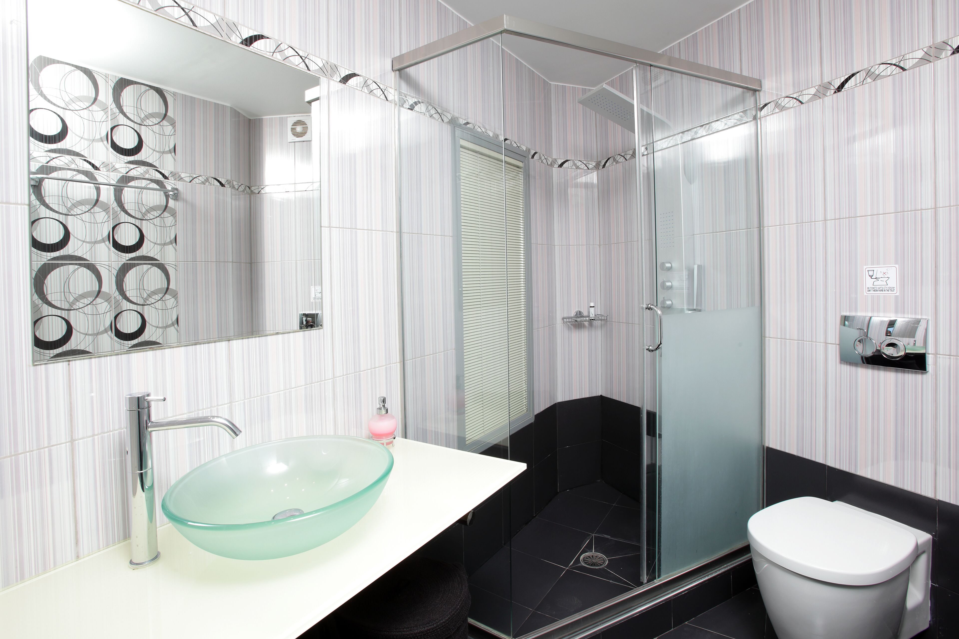 Une salle de bain moderne avec une douche à parois de verre, un lavabo blanc avec un receveur en verre et des toilettes.