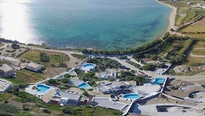 An aerial view of a coastal property with multiple swimming pools, a beach, and residential buildings. - Villa Paradise (Naxos)
