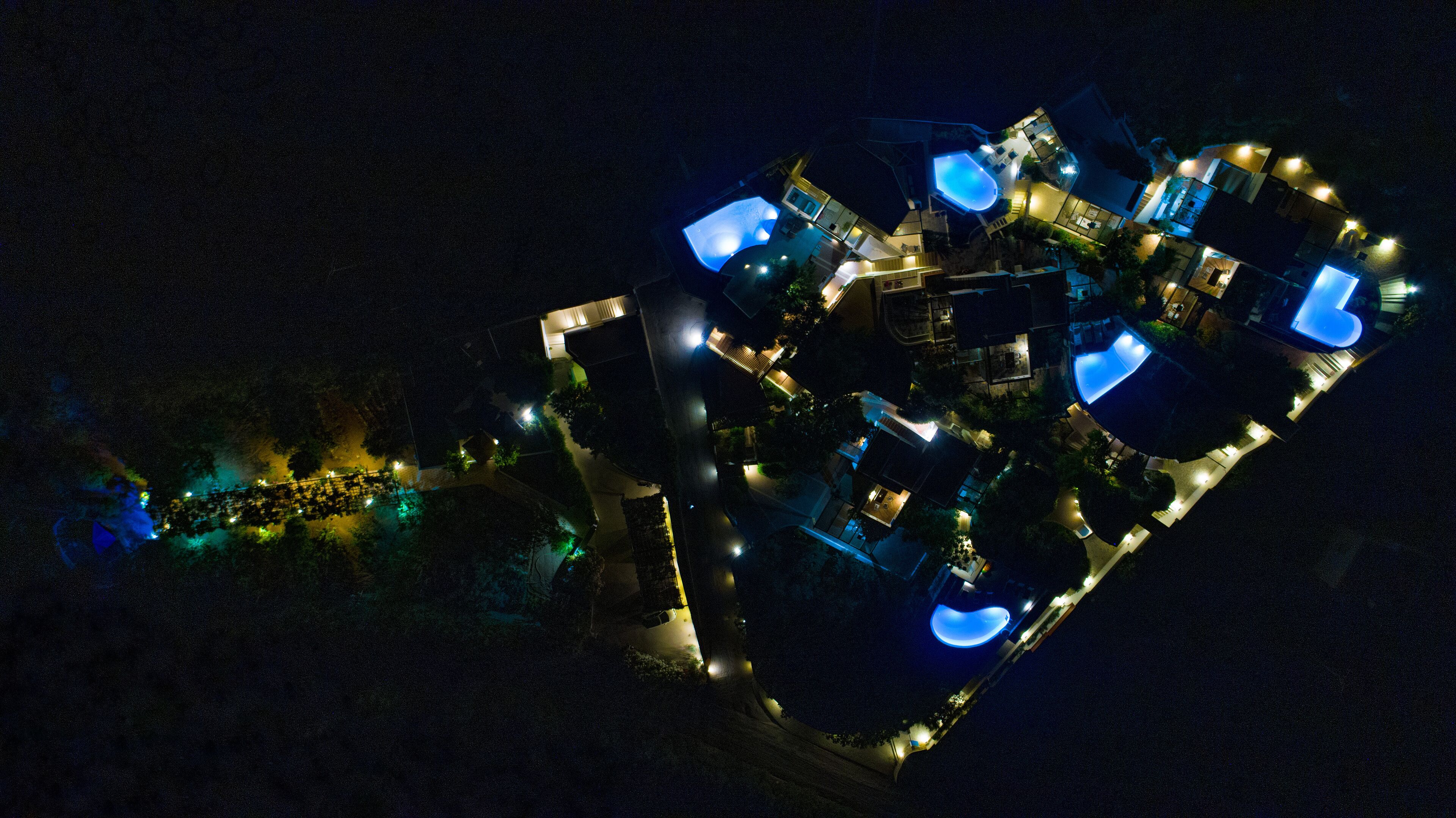 An aerial view of a resort with multiple swimming pools, connected by walkways, and surrounded by landscaped areas.