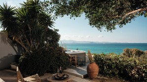A patio with wicker chairs, a table, and a hot tub overlooking a clear blue sea. - Villa Paradise (Naxos)