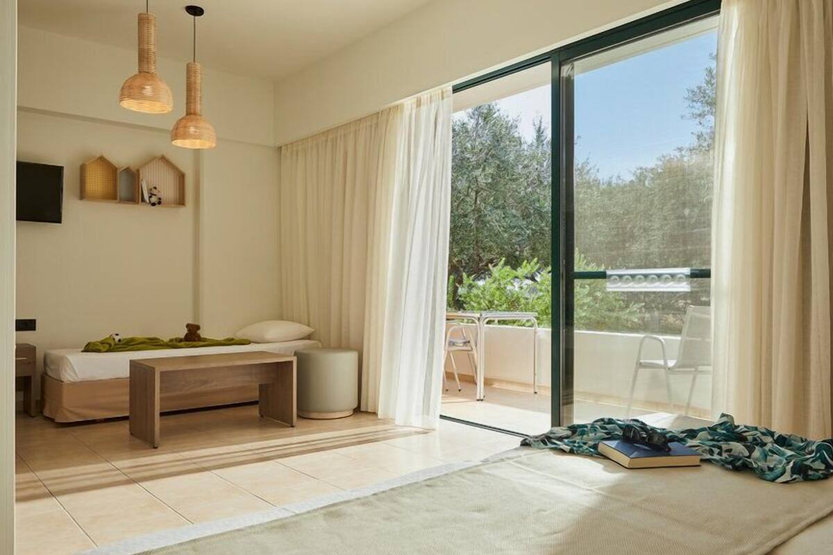 A modern bedroom with a bed, a small desk, and a balcony with a view of greenery.