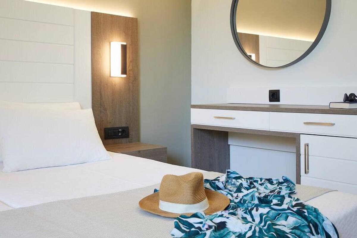 A hotel room with a bed, a bedside table, a mirror, and a dresser.