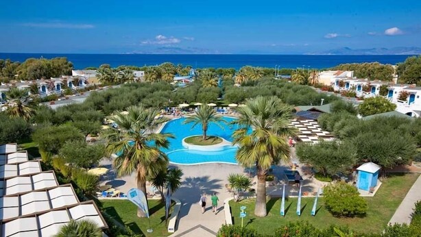 Un resort con piscina central rodeada de palmeras, zona de playa y vista al mar.