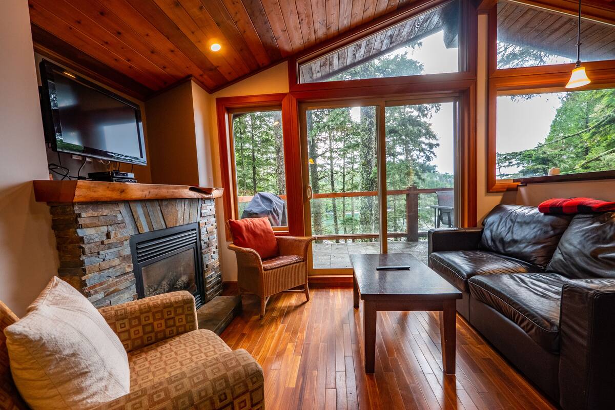 A cozy living room with a fireplace, wooden flooring, a leather sofa, and a television mounted on the wall.