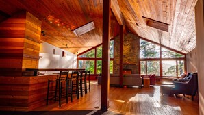Un interior amplio con techo de madera, ventanas grandes, chimenea de piedra y una zona de bar.