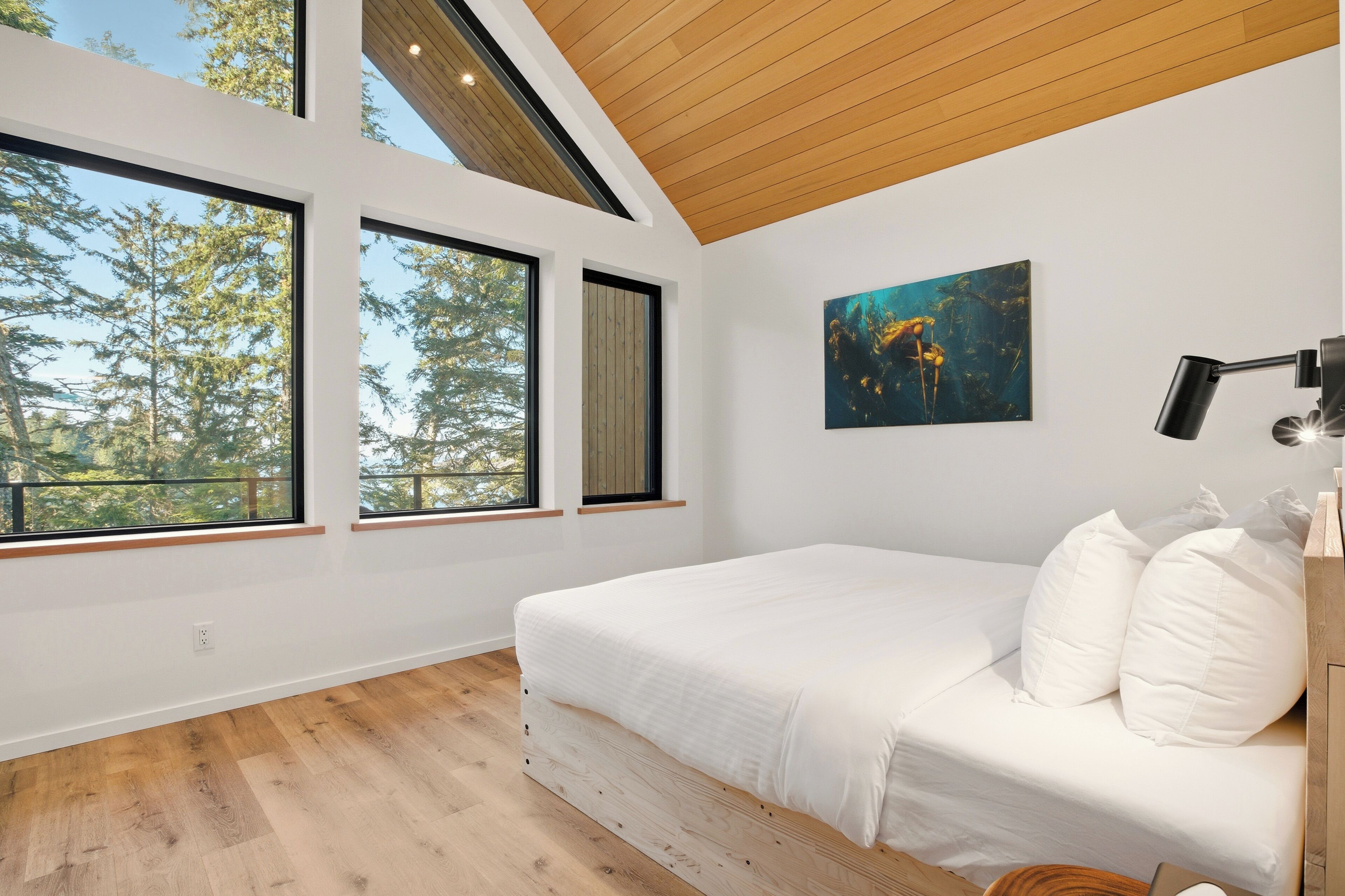 A bedroom with a large bed, multiple windows, a painting, and a desk lamp.