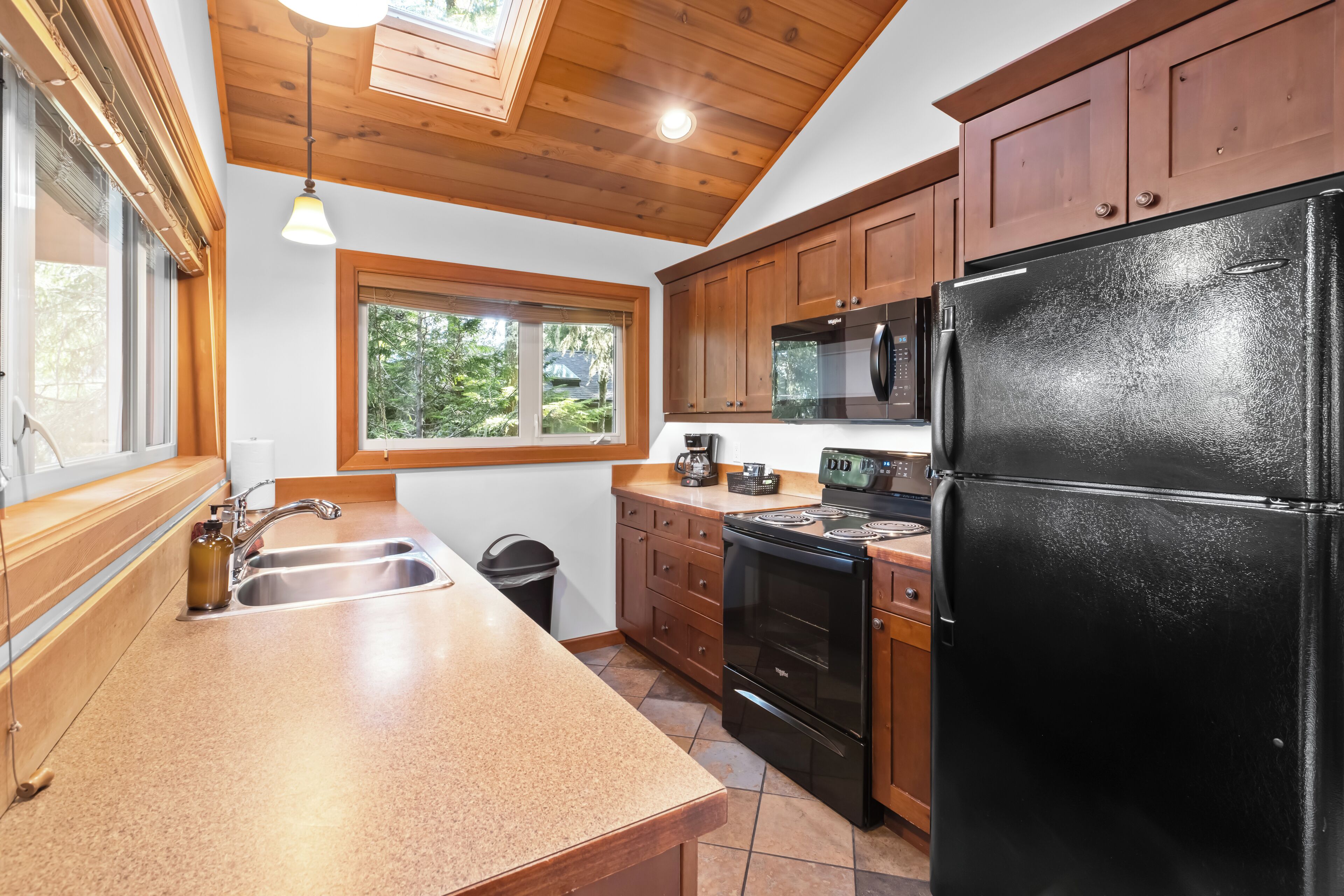 Una cocina con armarios de madera, un refrigerador negro, una estufa y un ventanal que proporciona luz natural.