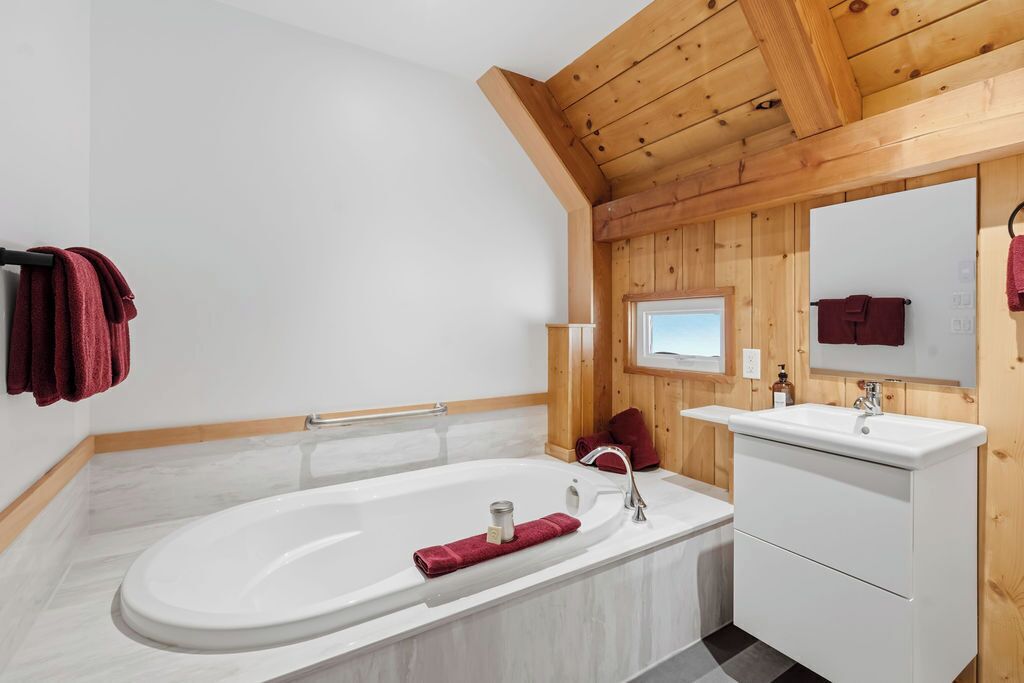 Un baño moderno con una bañera independiente, un tocador con espejo y paneles de madera en las paredes.