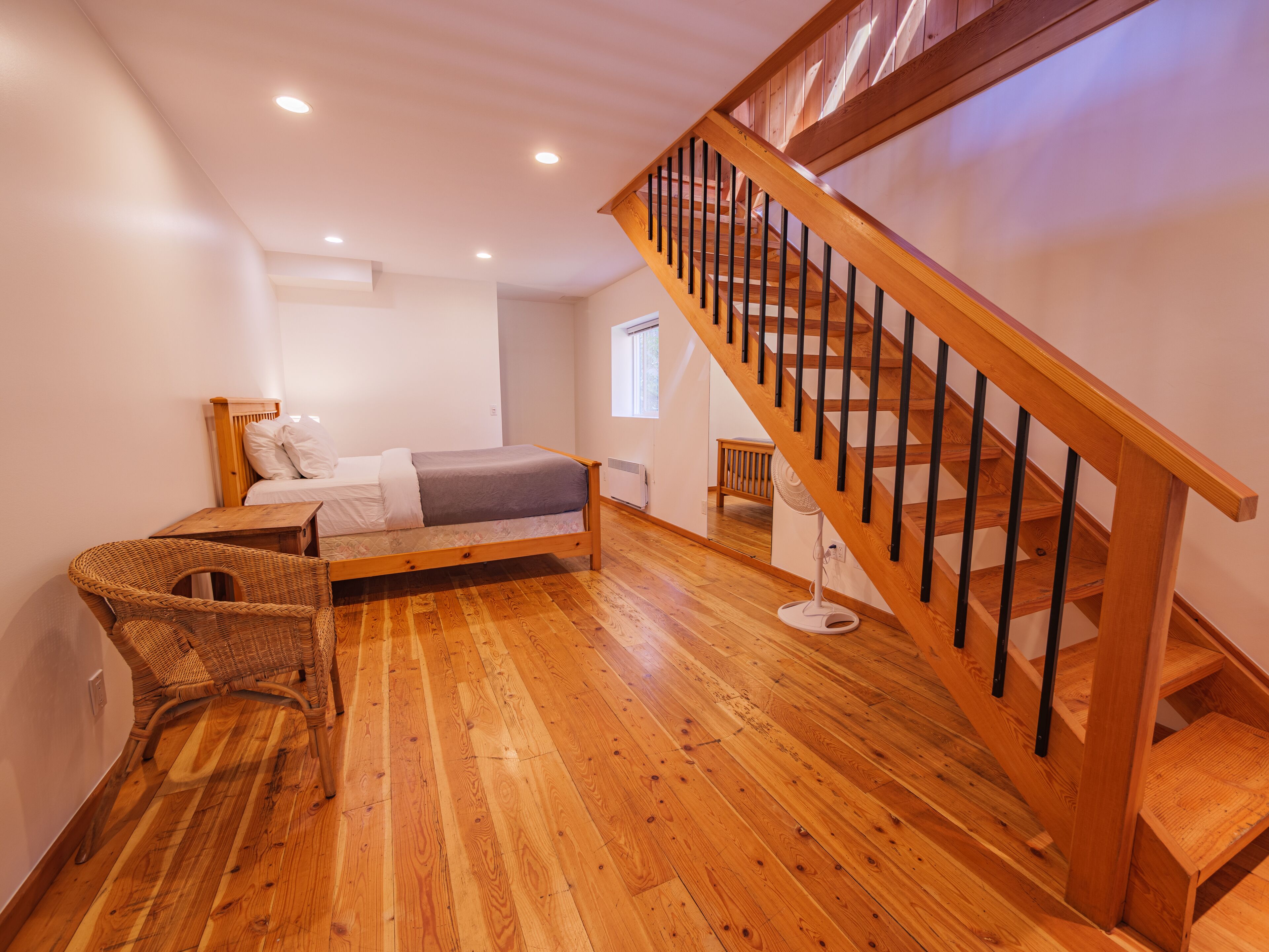 A bedroom with a wooden bed, a wooden staircase, and a wicker chair.
