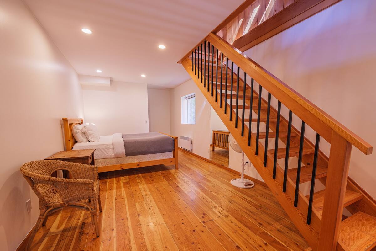 A bedroom with a wooden bed, a wooden staircase, and a wicker chair.