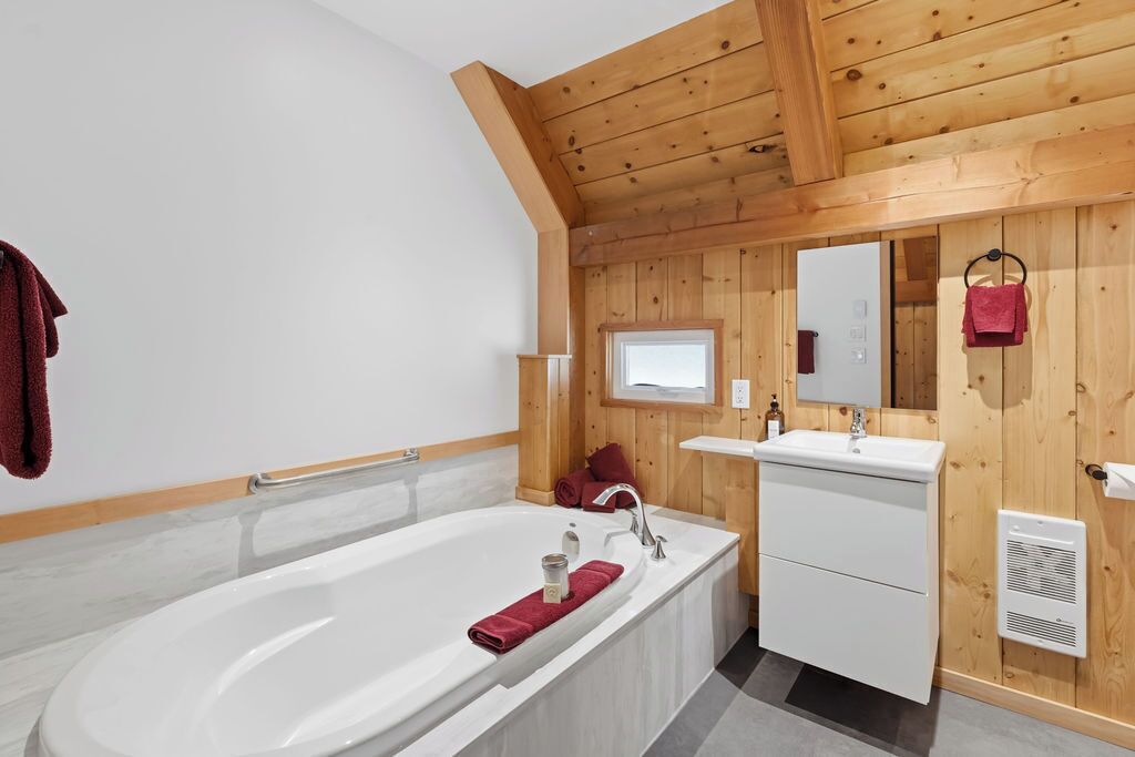 Ein modernes Badezimmer mit einer freistehenden Badewanne, einem Waschtisch mit Spiegel und Holzvertäfelung.
