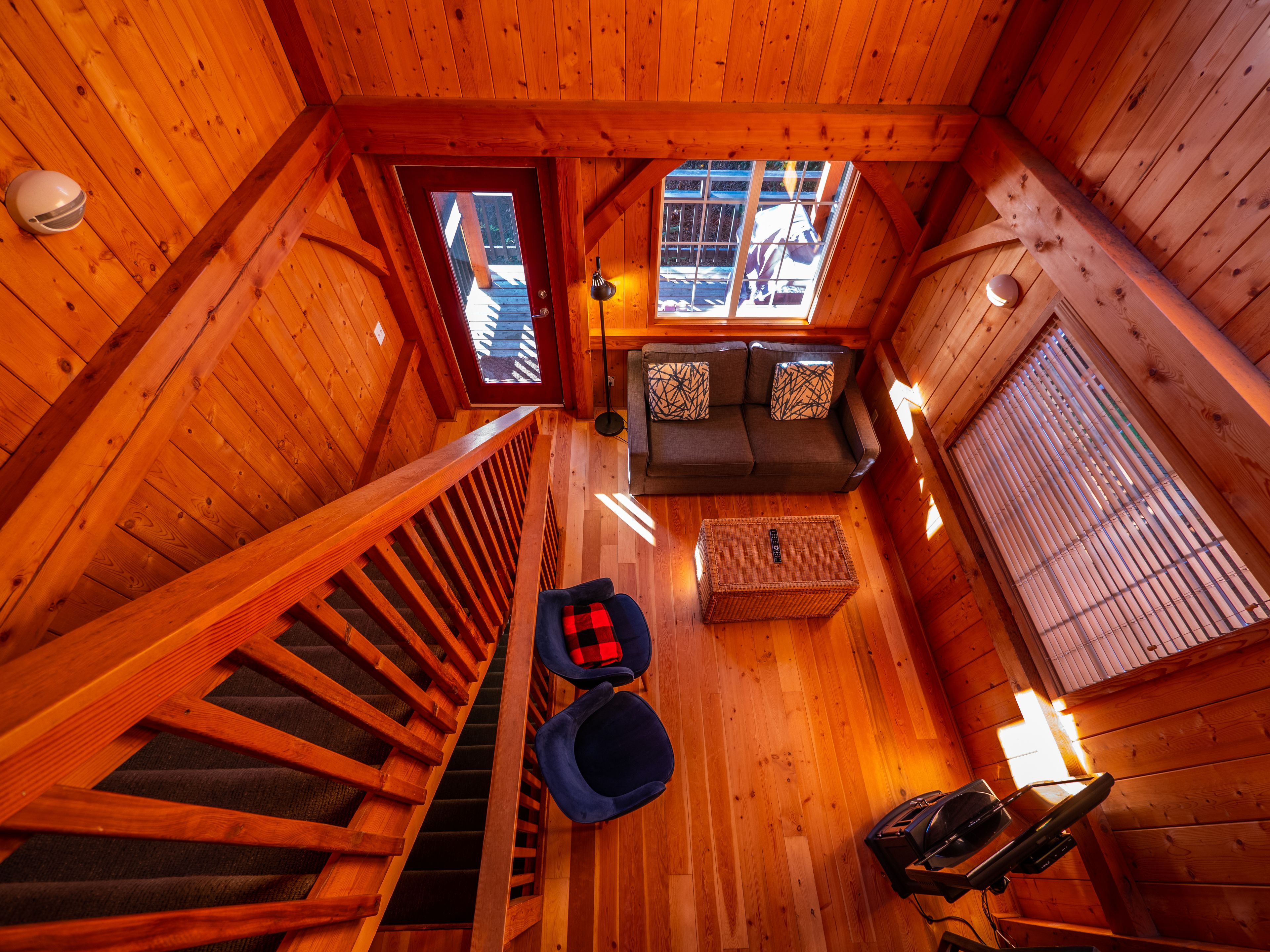 Une cabane en bois avec un escalier, un canapé, une petite table et une fenêtre.