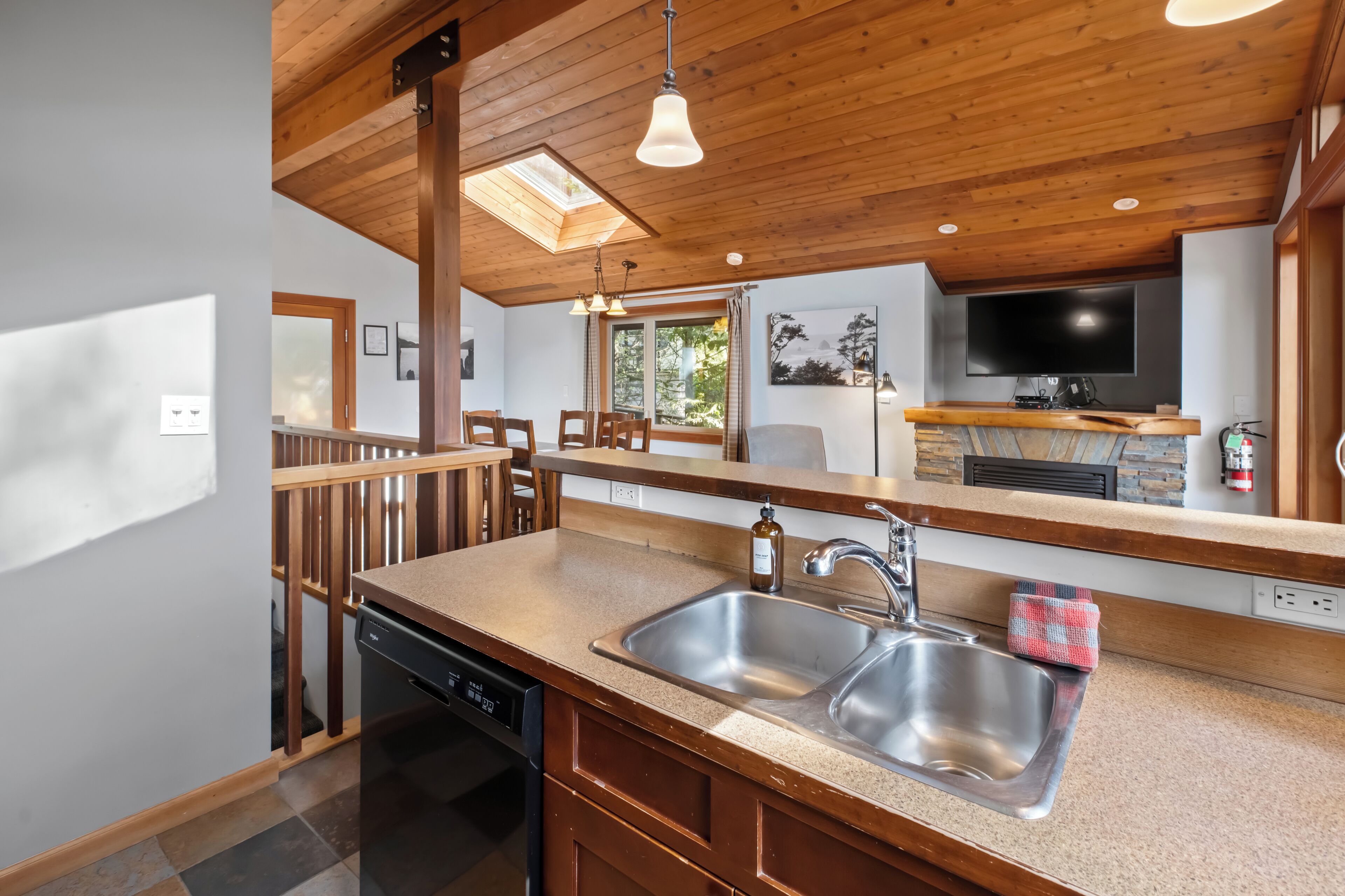 A modern kitchen with a wooden ceiling, skylight, stainless steel sink, and a flat-screen TV.