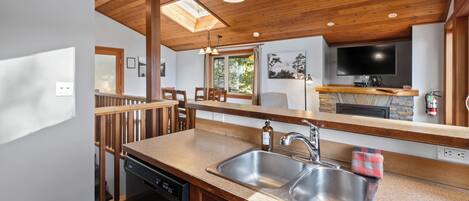 A modern kitchen with a wooden ceiling, skylight, stainless steel sink, and a flat-screen TV.