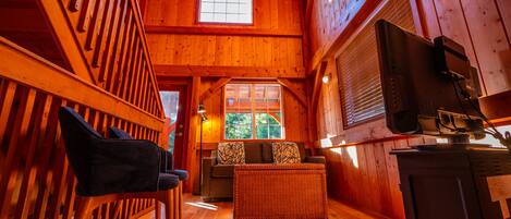 Un acogedor interior de cabaña con una escalera de madera, un sofá y un televisor.
