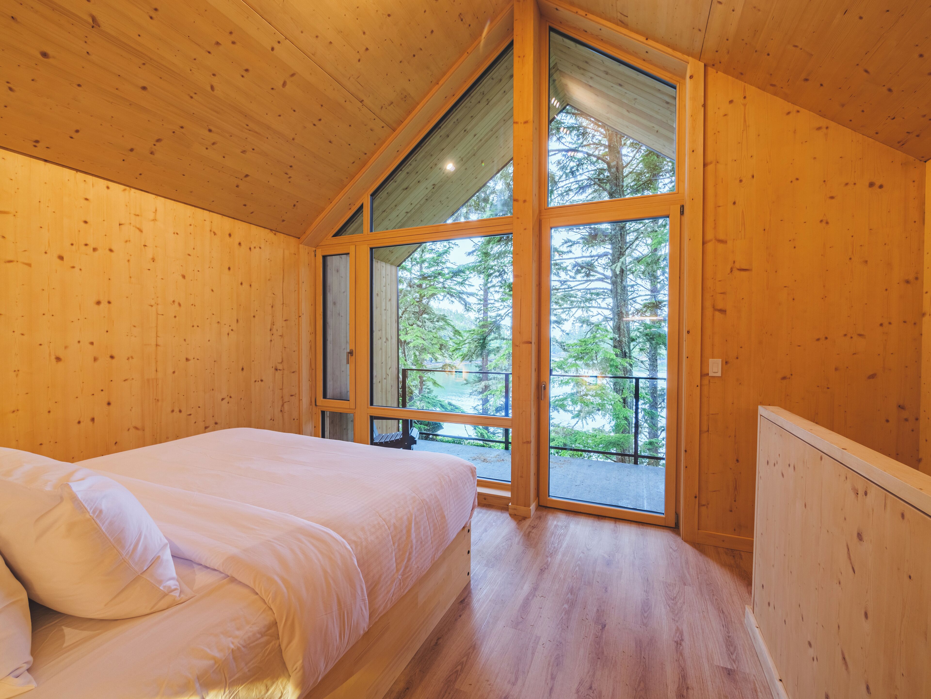 Ein Zimmer in einer Holzhütte mit einem Bett, großen Fenstern und Blick auf Bäume.