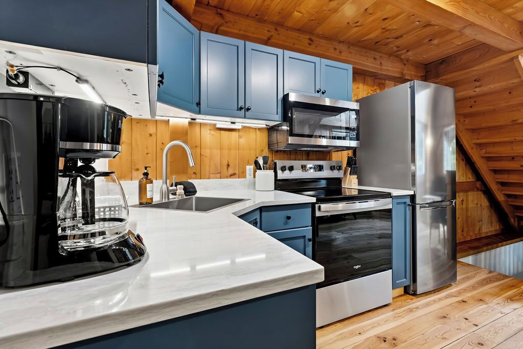 A modern kitchen with blue cabinets, stainless steel appliances, and a wooden ceiling.