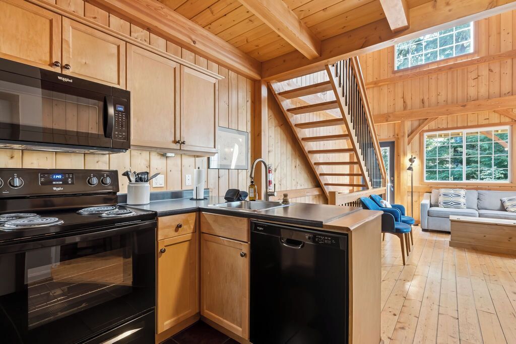 A wooden cabin interior with a kitchen, dining area, and a staircase.