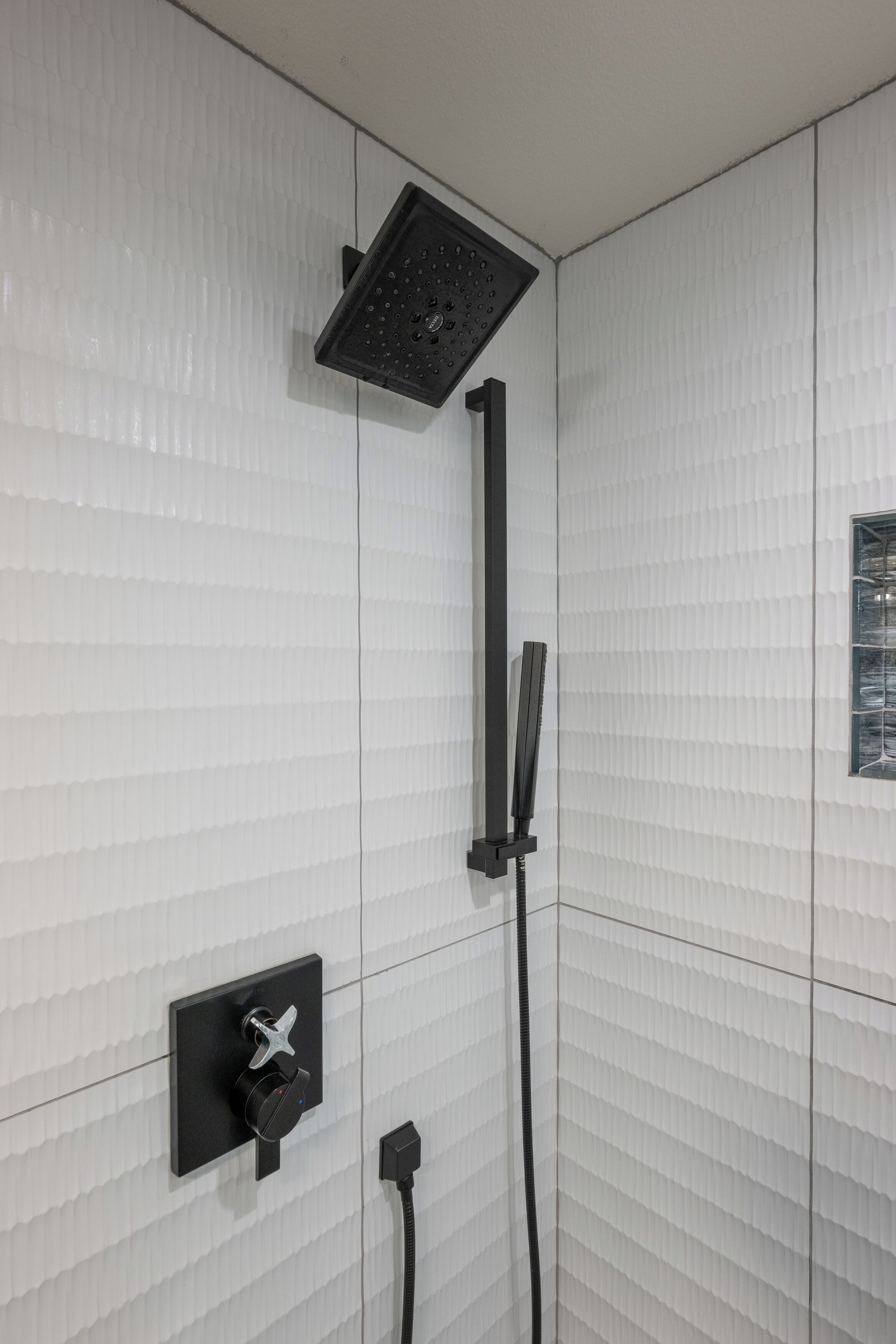 A shower with a black handheld showerhead and a wall-mounted control panel.