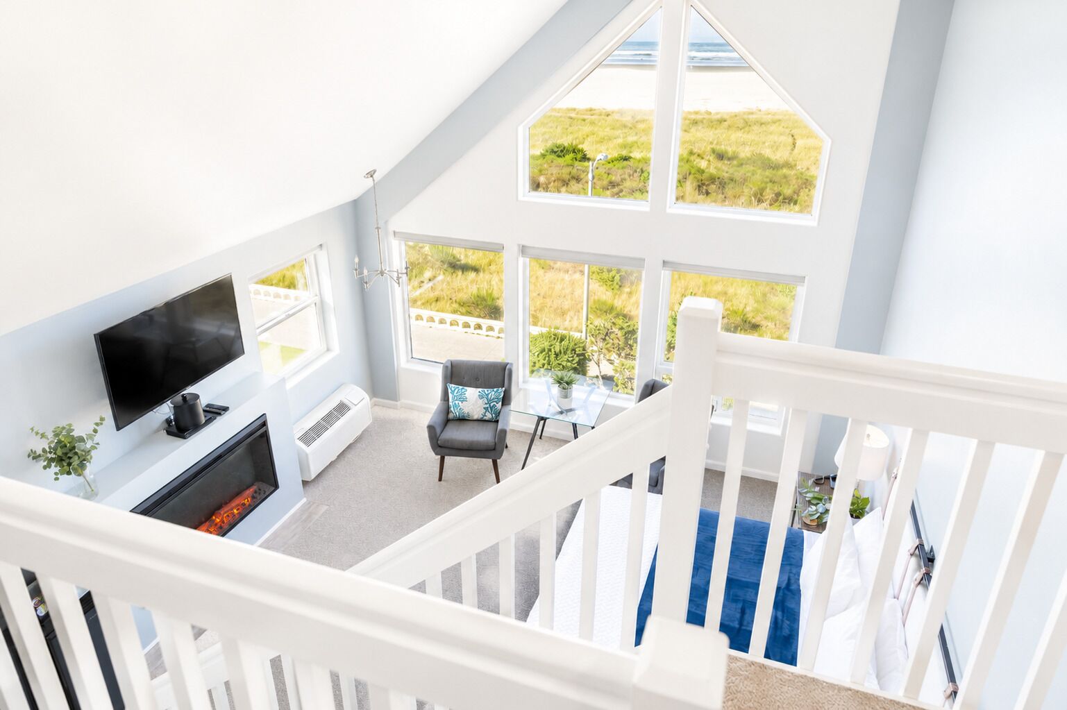 Ein Zimmer mit hohen Decken, einem Fernseher, einer Sitzecke und großen Fenstern mit Blick auf eine grüne Landschaft.