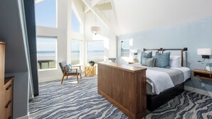 A bedroom with a large bed, a wooden desk, a chair, and a view of the ocean. - Seaside Oceanfront Inn (Seaside)