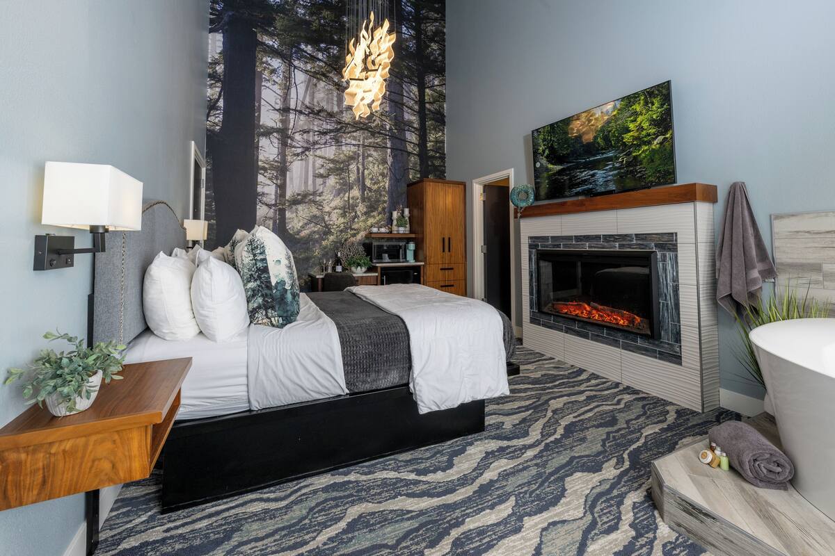 Un dormitorio moderno con una cama, chimenea, un mural grande en la pared y un televisor montado.