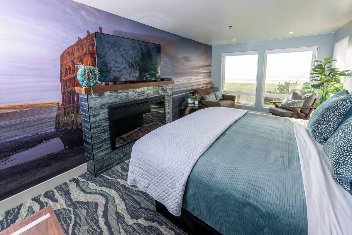 Un dormitorio con una cama grande, chimenea, televisor y vistas al exterior.