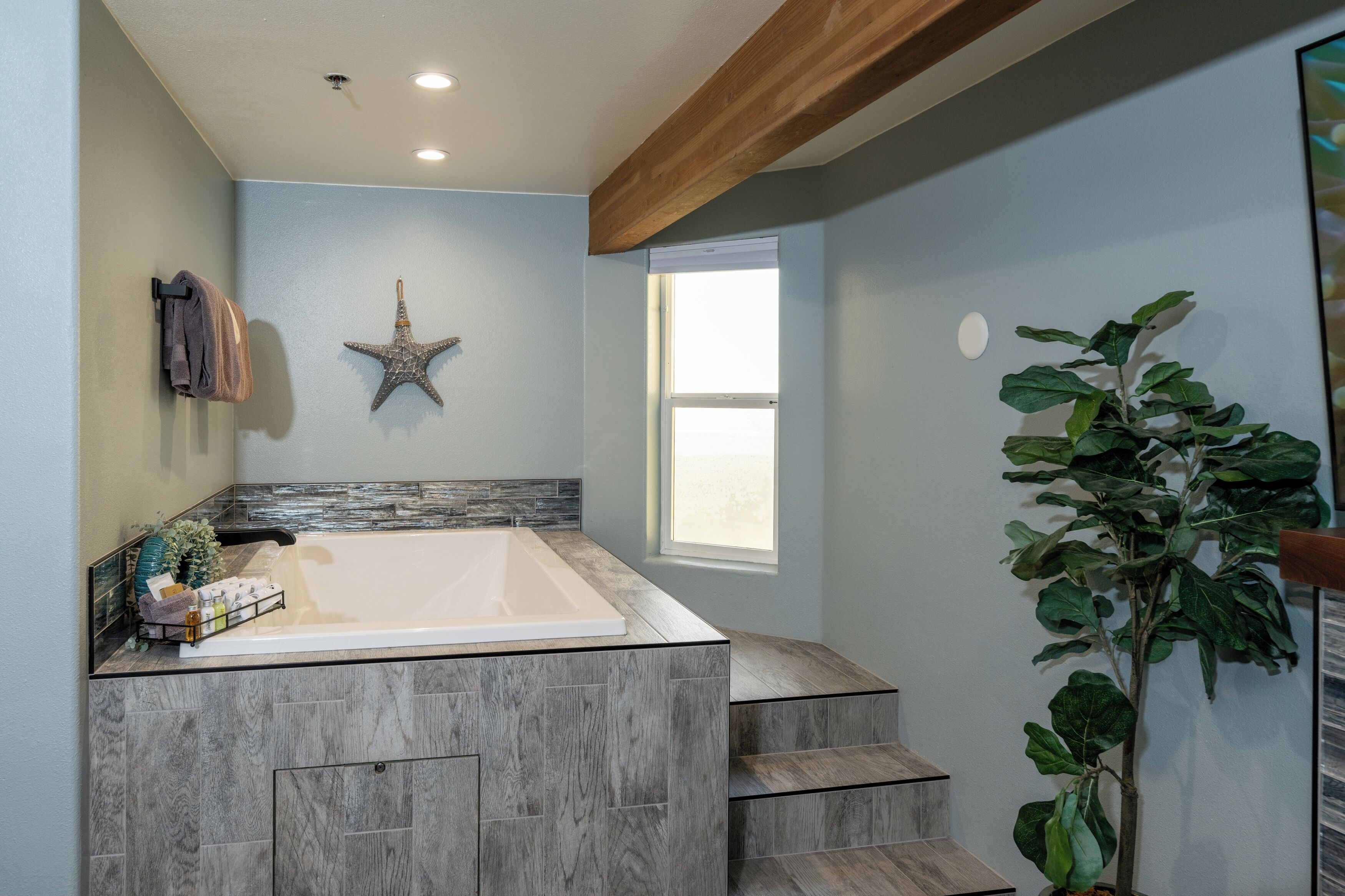 Une salle de bain dotée d’une grande baignoire, d’une décoration en forme d’étoile de mer et d  ’une fenêtre laissant entrer la lumière naturelle.