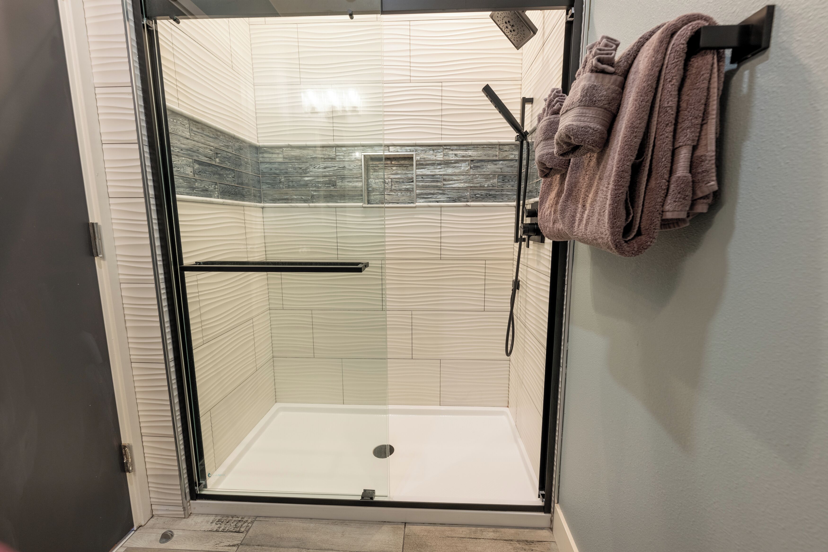 A glass-enclosed shower with a tiled wall and a towel rack with towels.