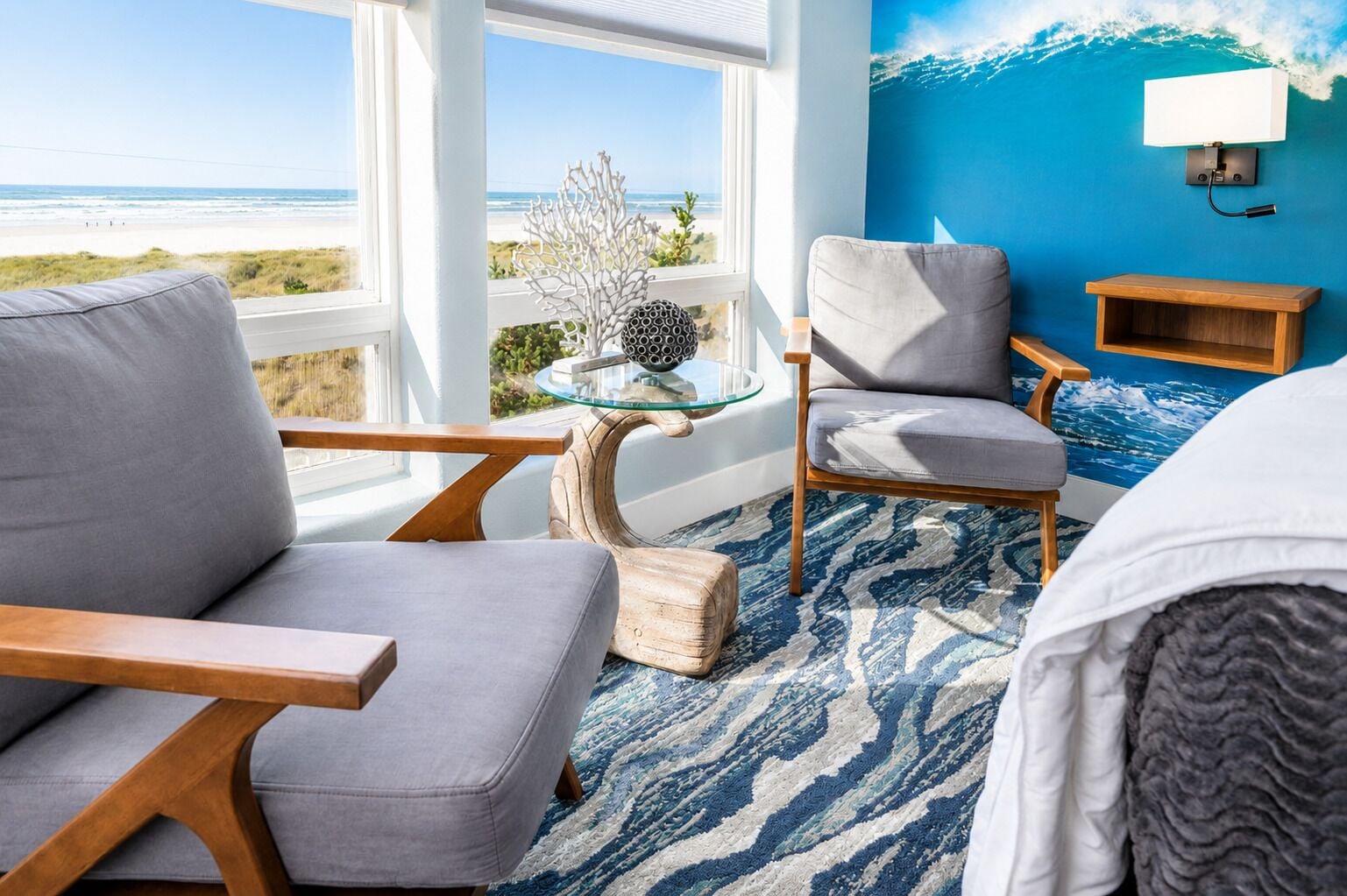 A room with a view of the beach, a blue wall, a white bed, and a grey sofa.