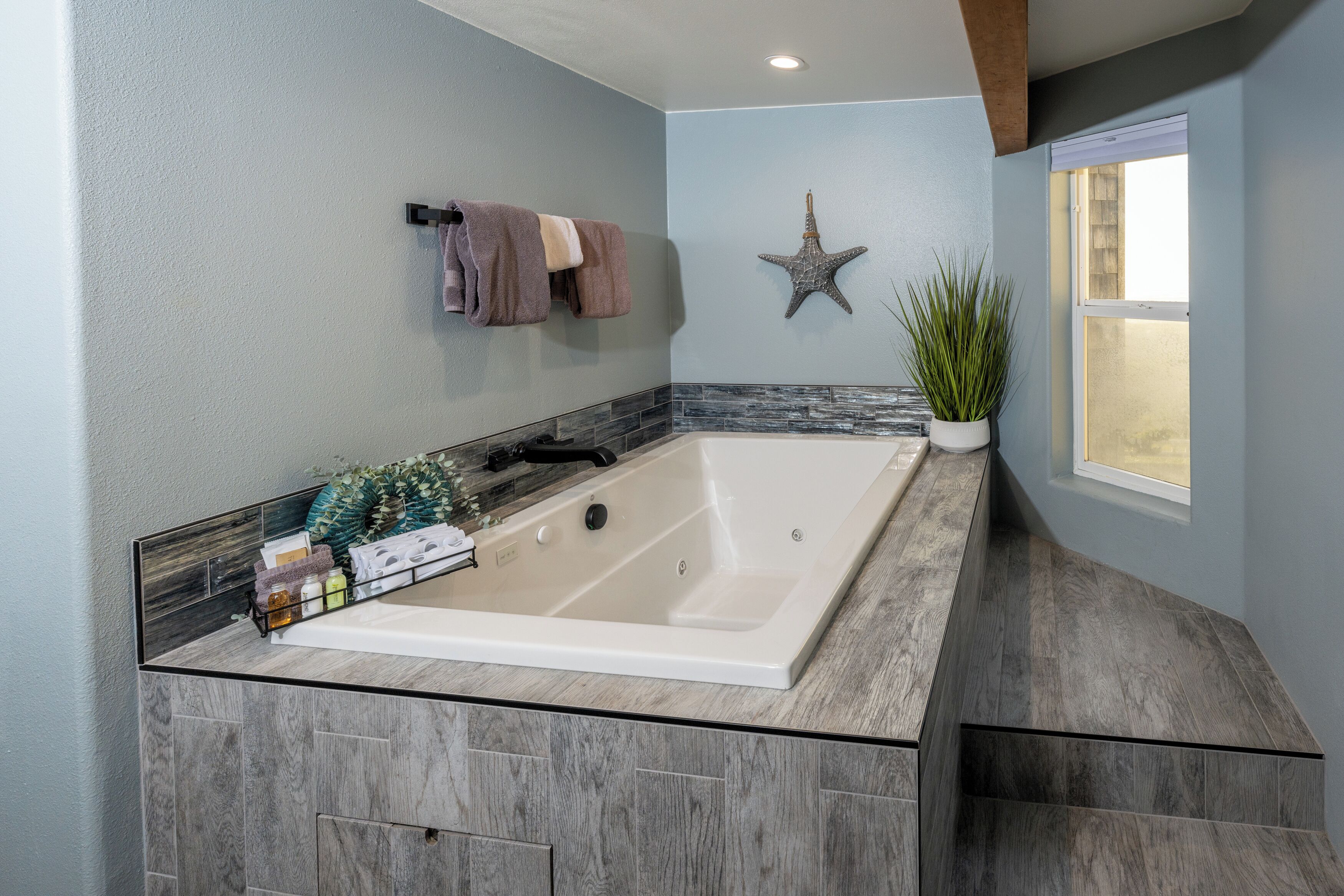 Un bagno moderno con una vasca da bagno grande, una decorazione a stella marina e una pianta in vaso.