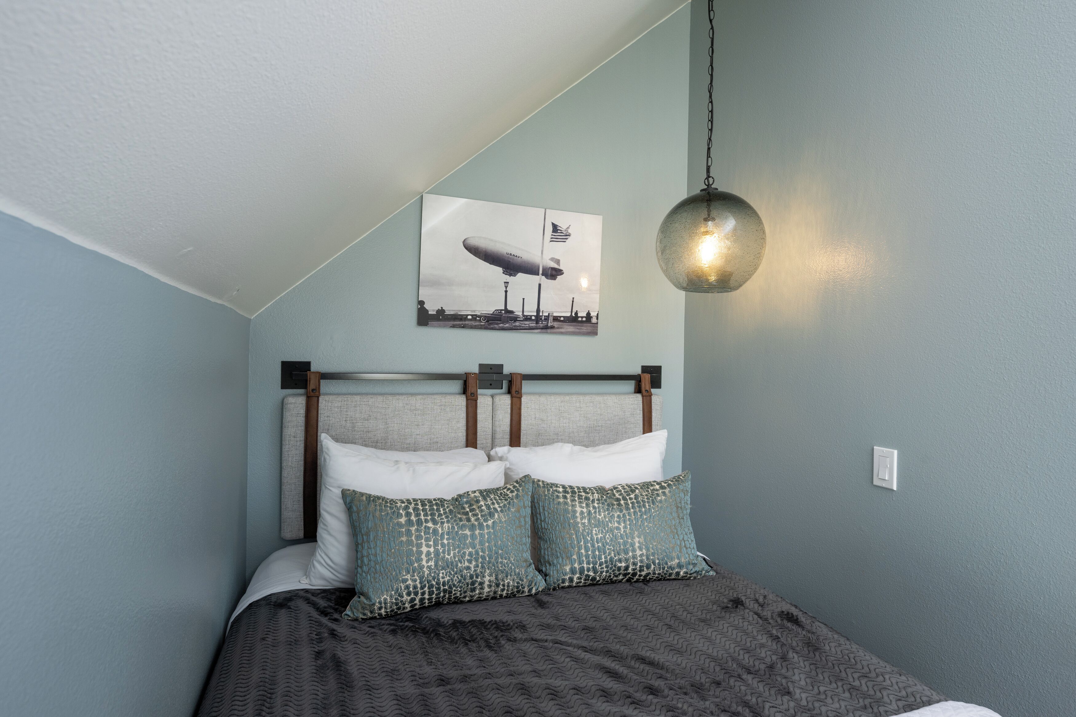 A bedroom with a bed, pillows, a hanging light fixture, and a wall-mounted picture.